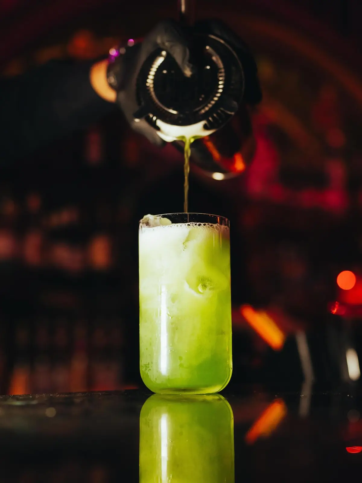 A green cocktail being poured at the bar