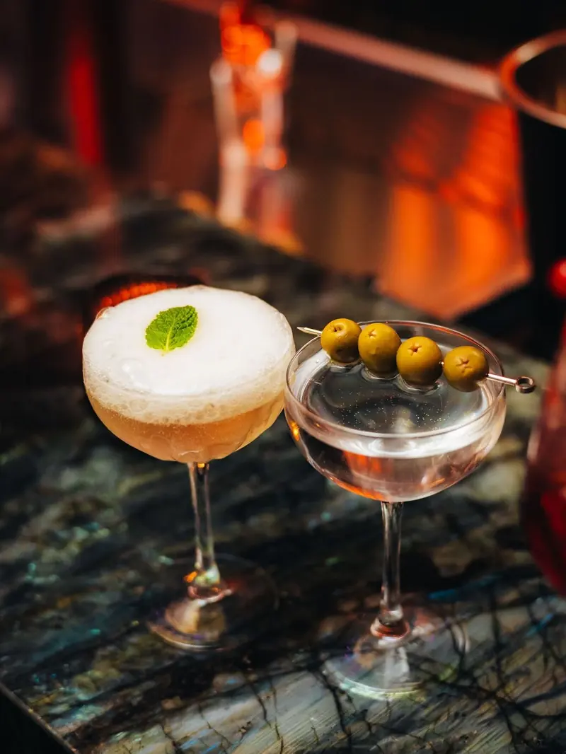 A sour and a martini with olives on the marble bar